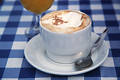 Tasse Cappuccino mit Sahne Foto auf karierter Tischdecke Café Warmgetränk