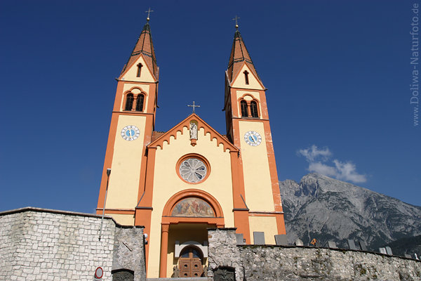 Telfskirche historischer Sakralbau Doppeltürme über Mauer vor Berg Blauhimmel-Hintergrund