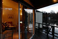 512026_Bungalow Innen mit Holzbalkon Bild mit Ausblick hinter grossen Glaswand auf Wasserlandschaft