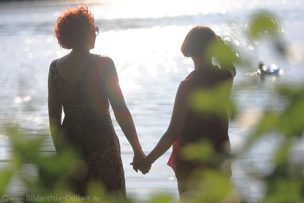 Jenseitslicht Sonnenreflexe ber Frauenpaar Silhouetten Hand in Hand am Wasser
