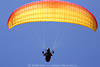 1202412_Gleitschirmvollbreite Flugfoto rot-gelb am Himmel in Blau ber Pilot mit Leinen in Hnden